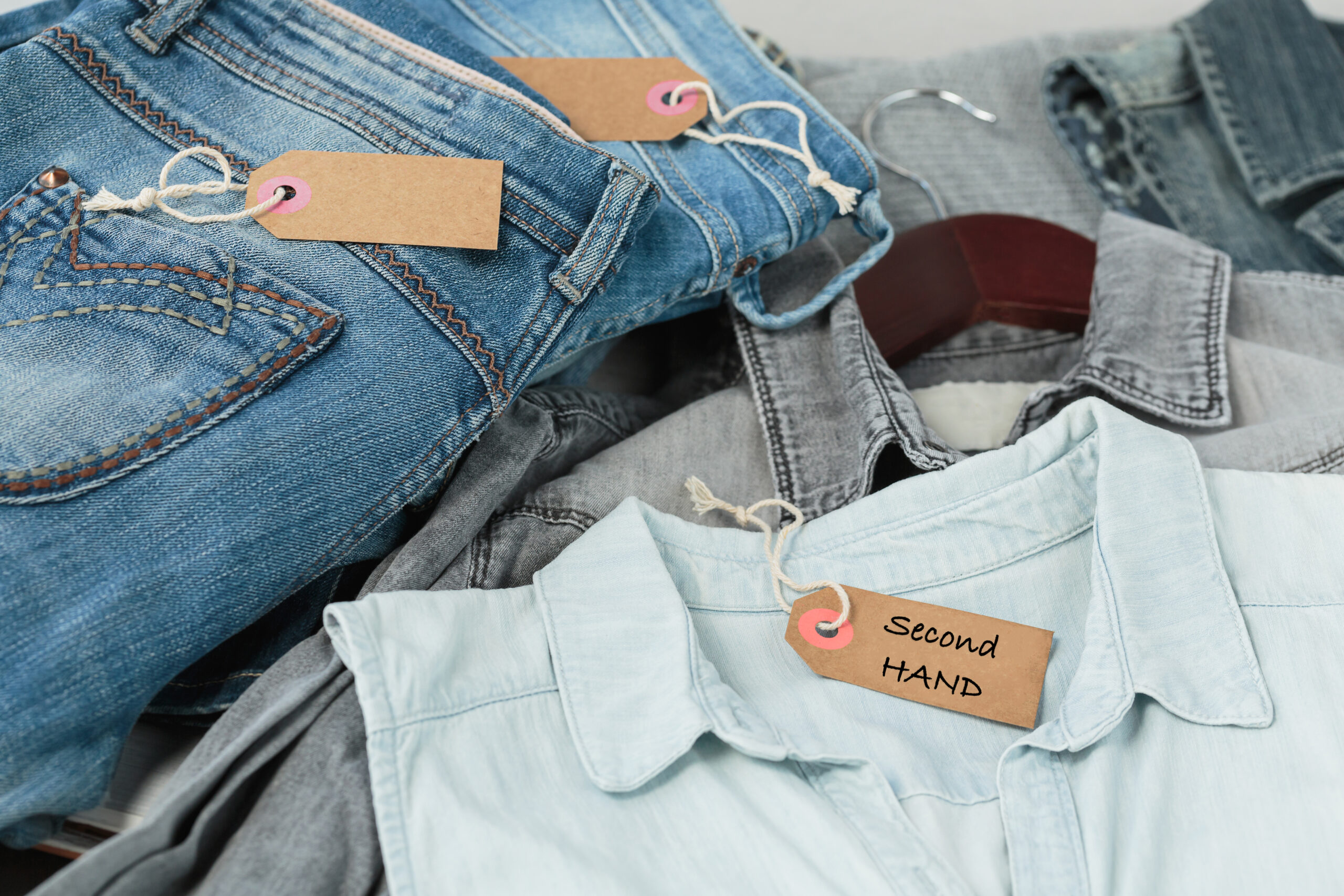 Stack of blue jeans, shirts and tag with inscription second hand. Second hand clothing shop. Circular fashion, eco friendly sustainable shopping, thrift stores concept. Top view over woman outfit